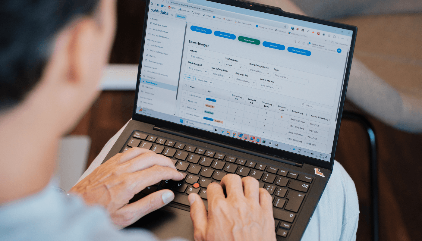 Eine Person sitzt vor einem Laptop und betrachtet eine Übersicht im publicjobs.ch-System. Auf dem Monitor sind verschiedene Funktionen sichtbar. Die Aufnahme zeigt die Person von hinten.