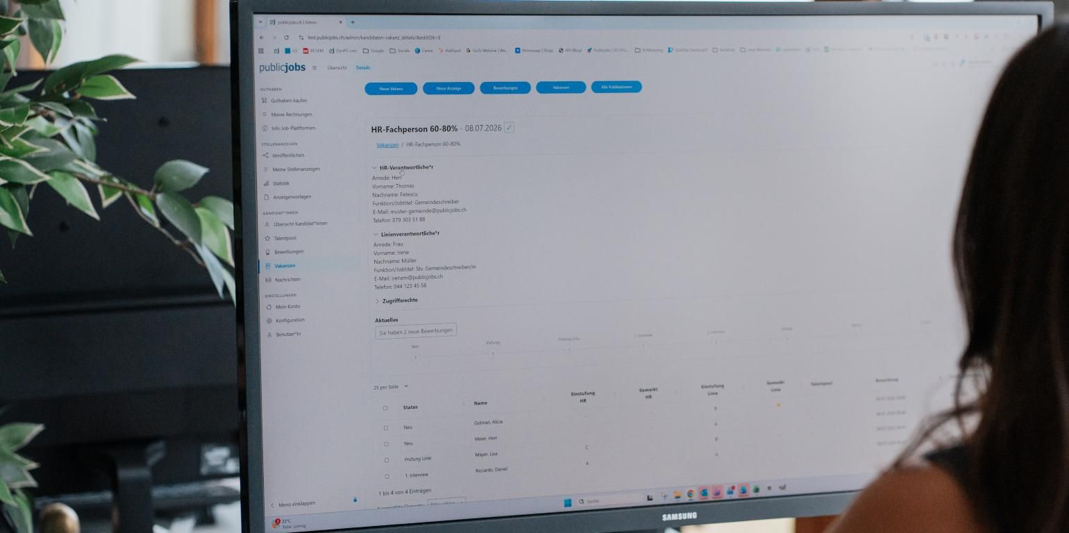 Eine Person sitzt vor einem grossen Bildschirm und arbeitet im Publicjobs Login-Bereich. Ansicht der Bewerbungsübersicht im ATS mit einer tabellarischen Liste von Kandidat*innen, Statusangaben, Einstufungen und Tags. Die Person ist von hinten zu erkennen.