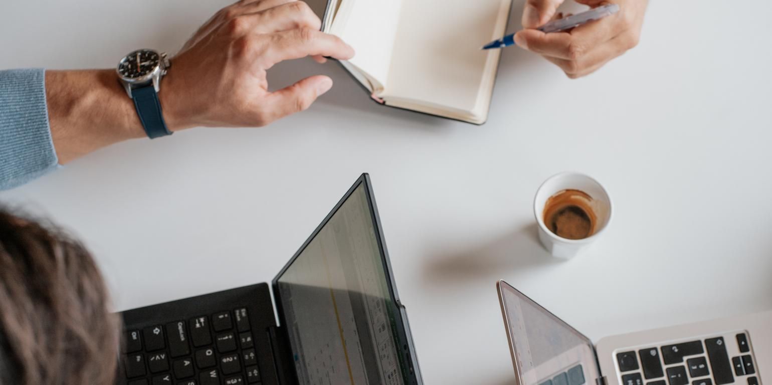 Besprechungssituation am Tisch mit mehreren Laptops, Notizbuch und Kaffee, passend zum Thema einfache Abrechnung und eine Sammelrechnung pro Schaltung auf der Stellenplattform publicjobs.ch.